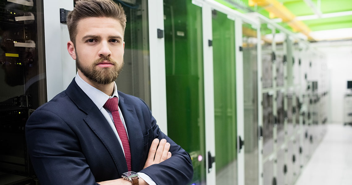 Man in a business suit standing with arms crossed in a server room. Text overlay: "Xentara secures our IIoT infrastructure, protecting data integrity and reinforcing trust in the digital age."