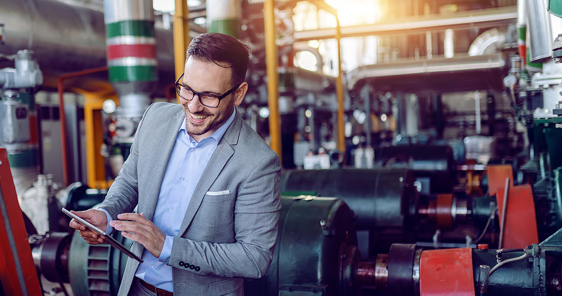 Person in a suit holding a tablet in an industrial setting. Text overlay: "Using Xentara-based controls we can push new machine features to customers with a simple code update."