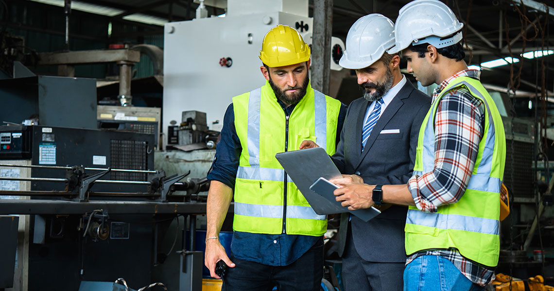 Three workers in hard hats and safety vests discussing with a tablet in an industrial setting. Text overlay: "Using Xentara's Virtual Commissioning features allowed us to cut our startup operations time in half."