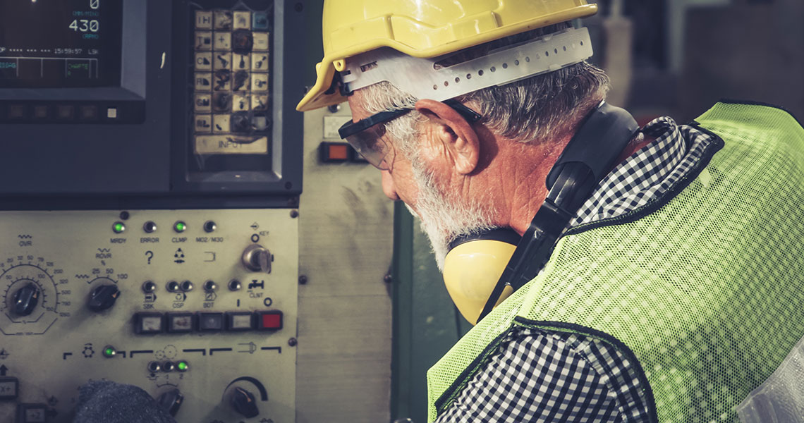 A worker in a hard hat and reflective vest operating machinery with dials and buttons. The worker is middle aged, the machinery is visibly old. Text overlay: "You can’t build a real “smart factory” based on technology from the 1970s. But you can retrofit Brownfield machines with Xentara."