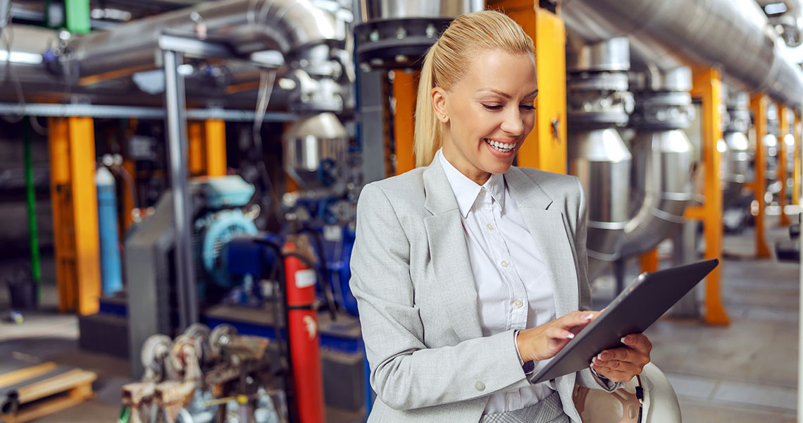 Businessperson with a tablet at an industrial facility. She seems happy about the information on her tablet. Text overlay: " Transitioning to new technologies is costly. Xentara bridges the gap between PLCs and smart services, simplifying the process."