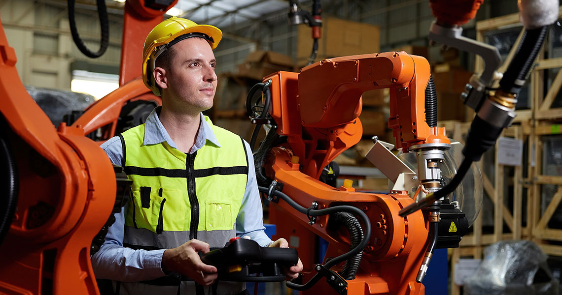 Person in a high-visibility vest and hard hat operating an industrial robot arm in a factory setting. Text overlay: "Pushing function blocks is so 20th century. Now we create our control code in high level programming languages. Xentara handles the rest."